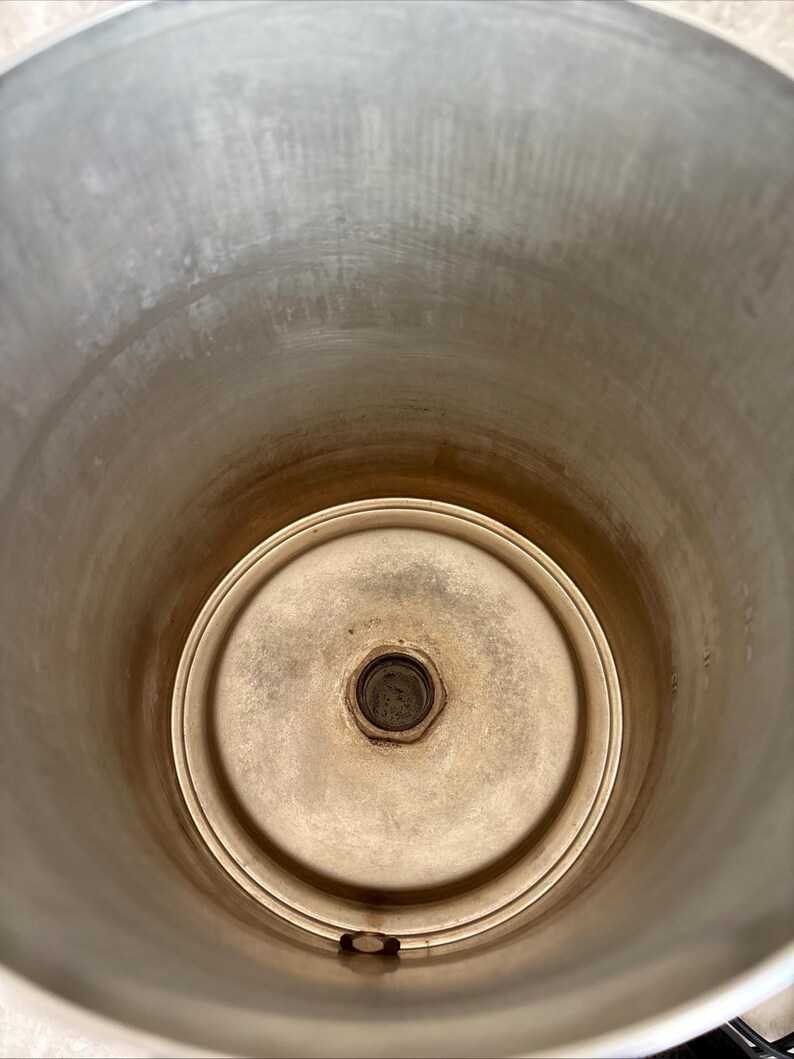 Puede incluir: Un recipiente cil&iacute;ndrico de acero inoxidable con base circular. El interior muestra signos de uso con algo de decoloraci&oacute;n. El recipiente tiene una abertura ancha y un accesorio central en la base.