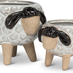 May include: Two ceramic sheep planters. The planters are white with a textured pattern, brown legs, and black accents. The sheep have tan faces and black ears. One planter is larger than the other.