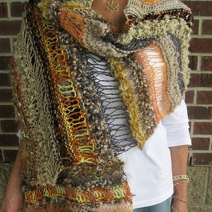 May include: A hand-knitted shawl in a mix of earthy tones, including brown, orange, and yellow. The shawl has a variety of textures, with open-weave and knitted sections. The garment is draped over the shoulders, showcasing its intricate design.