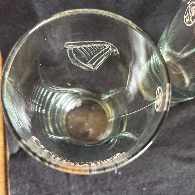 May include: Clear glass drinking glasses with a logo etched on the side. The glasses have a wide, rounded shape and a thick base. The logo appears to be a stylized bird or wing design. The word "Guinness" is printed on the side of the glass.