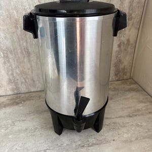 Puede incluir: Una cafetera de acero inoxidable con tapa, asas y base negras. La cafetera tiene un grifo para dispensar. El exterior est&aacute; pulido y es reflectante. Ideal para servir caf&eacute;.