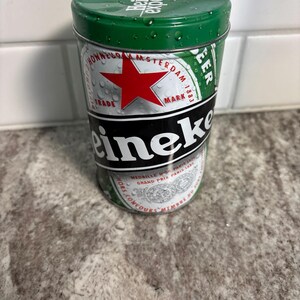 May include: A cylindrical Heineken beer can with a green lid and a silver body. The can features the Heineken logo, a red star, and the words "Heineken experience". The can is covered in water droplets.