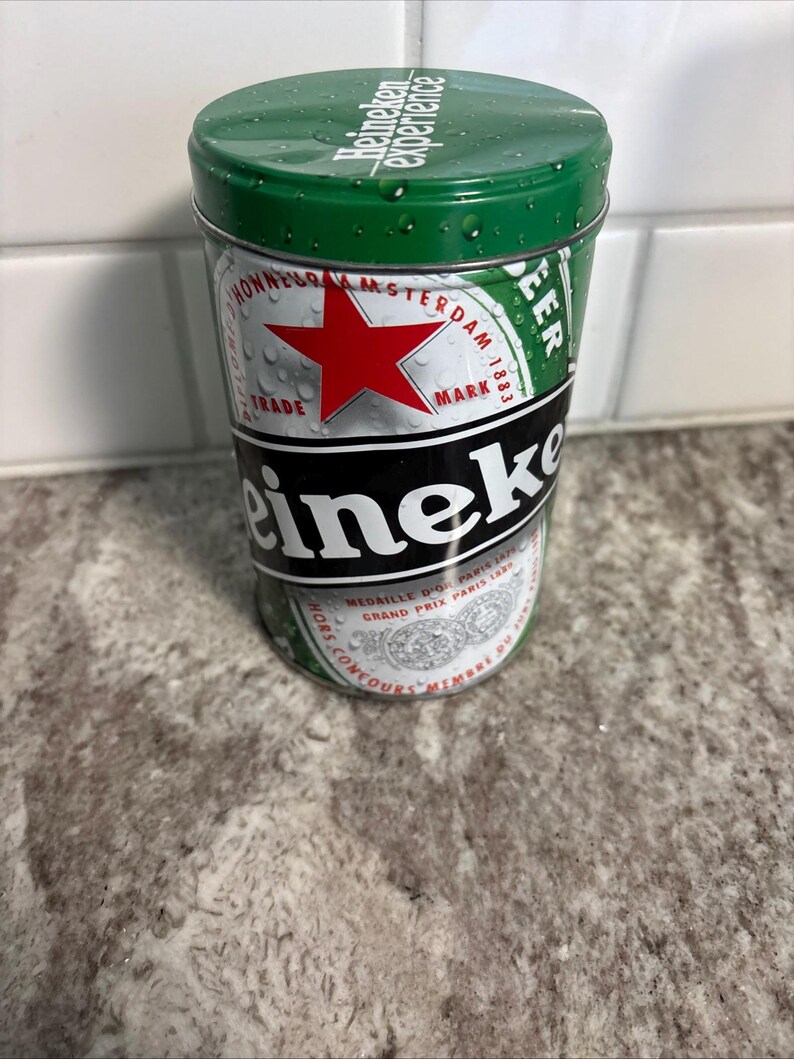 May include: A cylindrical Heineken beer can with a green lid and a silver body. The can features the Heineken logo, a red star, and the words "Heineken experience". The can is covered in water droplets.