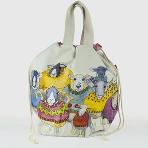 May include: A white canvas drawstring bag with a colorful illustration of sheep wearing sweaters. The sheep are in various poses and have different colored sweaters. The bag has a white cotton handle.