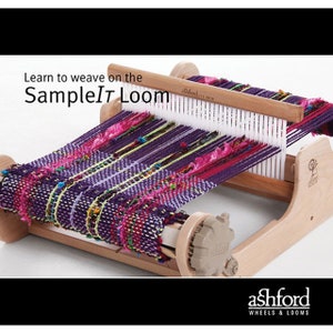 May include: A wooden SampleIt loom with a partially woven textile. The textile features purple, pink, and green threads. The text "Learn to weave on the SampleIt Loom" is displayed above the loom. The Ashford logo is at the bottom.