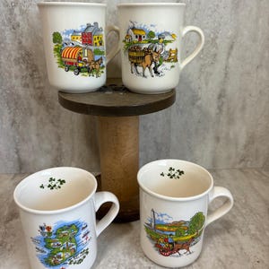 May include: Set of four white ceramic mugs with Irish themed illustrations. The mugs feature scenes of Irish countryside, a map of Ireland, and a donkey cart.