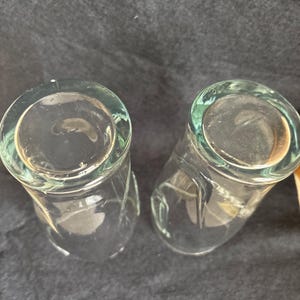 May include: Two clear, cylindrical drinking glasses. The glasses have a slightly flared rim and a rounded base. The glass is clear, allowing the contents to be visible. The glasses are likely used for beverages.