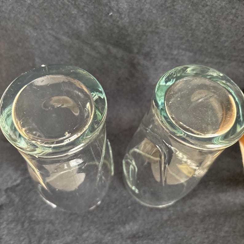 May include: Two clear, cylindrical drinking glasses. The glasses have a slightly flared rim and a rounded base. The glass is clear, allowing the contents to be visible. The glasses are likely used for beverages.