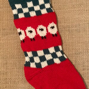 May include: A red, white, and green knitted Christmas stocking with a checkered pattern and a row of white sheep with black faces.