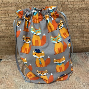 May include: A gray drawstring bag with a repeating pattern of orange foxes wearing glasses, hats, and ties. The bag has gray drawstrings.