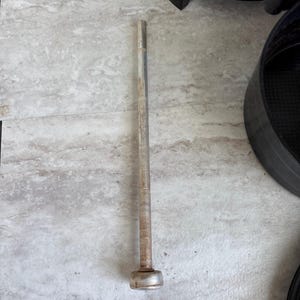 Puede incluir: Una larga varilla met&aacute;lica cil&iacute;ndrica con una base redondeada y ensanchada. La varilla tiene un aspecto ligeramente deslustrado y envejecido, lo que sugiere que puede ser vintage o usada. El objeto est&aacute; sobre una superficie clara y texturizada.