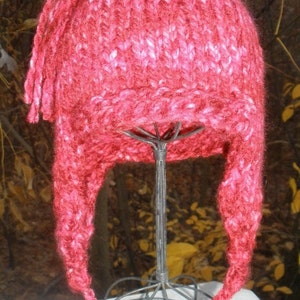 May include: A pink and red knitted hat with a long tassel. The hat is displayed on a wire stand.