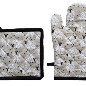 May include: A quilted oven mitt and pot holder set. The set features a light gray background with a pattern of white sheep. The edges are trimmed with black fabric. The pot holder is square, and the oven mitt has a loop for hanging.