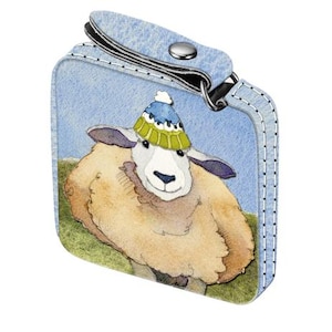 Op de afbeelding: Een blauwe leren sleutelhanger met een gestikte rand heeft een cartoon schaap met een blauwe en groene hoed.