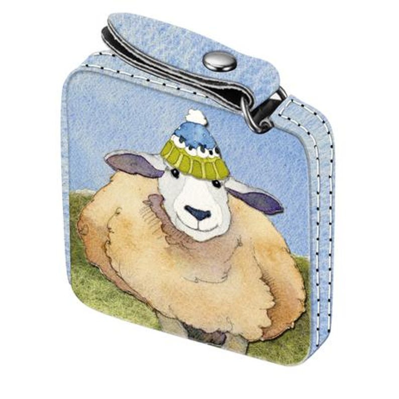 Op de afbeelding: Een blauwe leren sleutelhanger met een gestikte rand heeft een cartoon schaap met een blauwe en groene hoed.