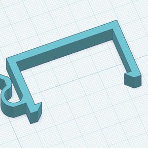 Pode incluir: Um suporte em forma de U de cor azul-clara, tridimensional, com uma barra superior plana e duas pernas voltadas para baixo. A perna esquerda apresenta um mecanismo de clipe curvo integrado, enquanto a direita termina numa borda reta simples.