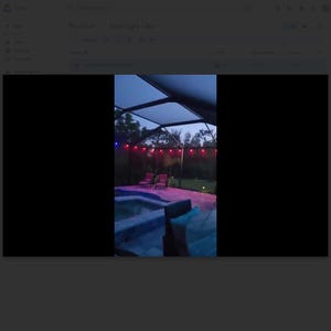 May include: Outdoor scene at dusk featuring a swimming pool, patio furniture, and string lights. The pool has blue and purple lighting. Red string lights are strung across the top of the patio. The sky is a dark blue.