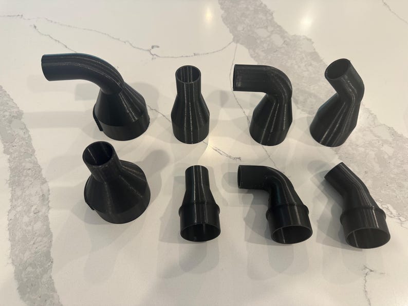 May include: Eight black plastic nozzles of varying shapes and sizes. Some are curved, others angled or flared. The collection is displayed on a white surface, showcasing the different designs and forms of the nozzles.
