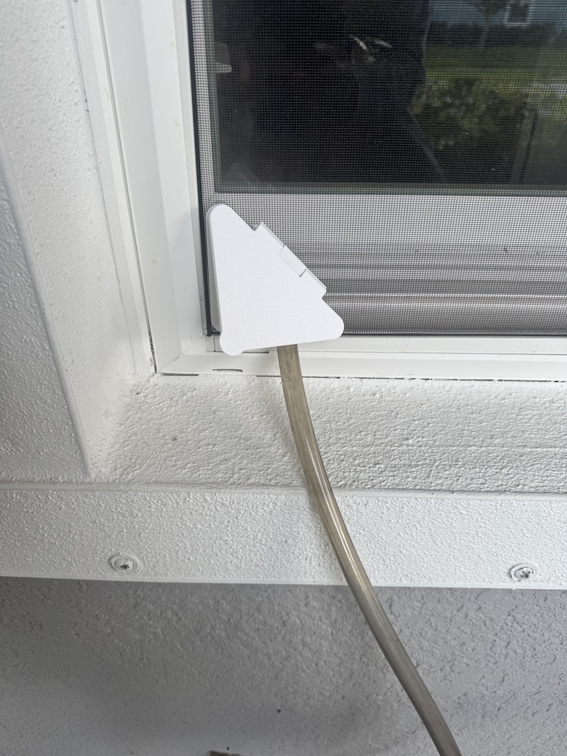May include: A white, triangular-shaped plastic window vent adapter plate installed in a window frame. A clear, flexible plastic hose is attached to the bottom of the adapter, extending downwards away from the window screen and frame assembly.
