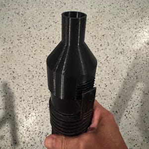 May include: A black, 3D-printed object with a cylindrical, ribbed handle and a flared top. The object has a rectangular clip and a series of ridges. The item is held in a hand.