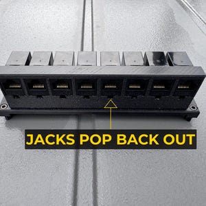 Peut inclure: Un panneau de brassage réseau noir imprimé en 3D avec huit ports Ethernet RJ45 disposés horizontalement. Une flèche jaune pointe vers les ports avec le texte JACKS POP BACK OUT affiché en lettres capitales jaunes sur fond noir.