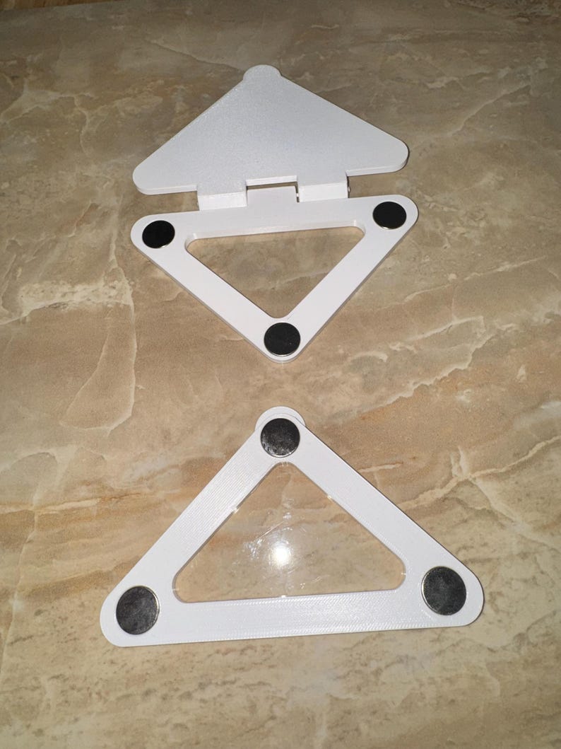 May include: Two white triangular stands with a smooth finish. Each stand features three circular black pads on the underside for stability. The top stand includes a hinged triangular flap attached to the base, while the bottom stand is a single frame.