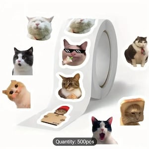 May include: A roll of stickers featuring various cat images. The stickers include a cat wearing sunglasses, a cat with a box on its head, a cat with a slice of bread on its head, and a cat with a tie. The text "Quantity: 500pcs" is printed on the roll.