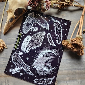 Könnte beinhalten: Ein schwarzes Stickerbogen mit weißen Illustrationen von Raben und Federn. Das Bogen enthält den Text "FA-CAW-F!" und die Website "christie-adams.com". Der Hintergrund ist schwarz mit weißen Sternen.