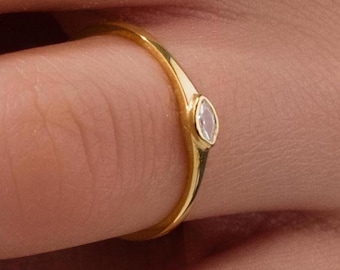 May include: A delicate gold ring with a single, small, clear gemstone set in the centre.