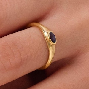 Könnte beinhalten: Ein goldener Ring mit einem kleinen, ovalen, dunkelblauen Edelstein, der in der Mitte eingesetzt ist.