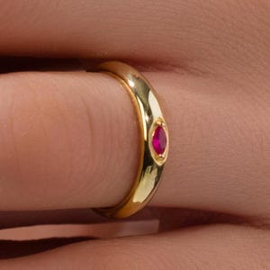 Könnte beinhalten: Ein Goldring mit einem einzigen roten Edelstein in der Mitte.