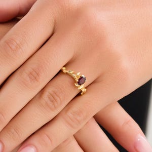 Pu&ograve; includere: Un anello d'oro con una pietra preziosa rossa incastonata in un delicato design a ramo.