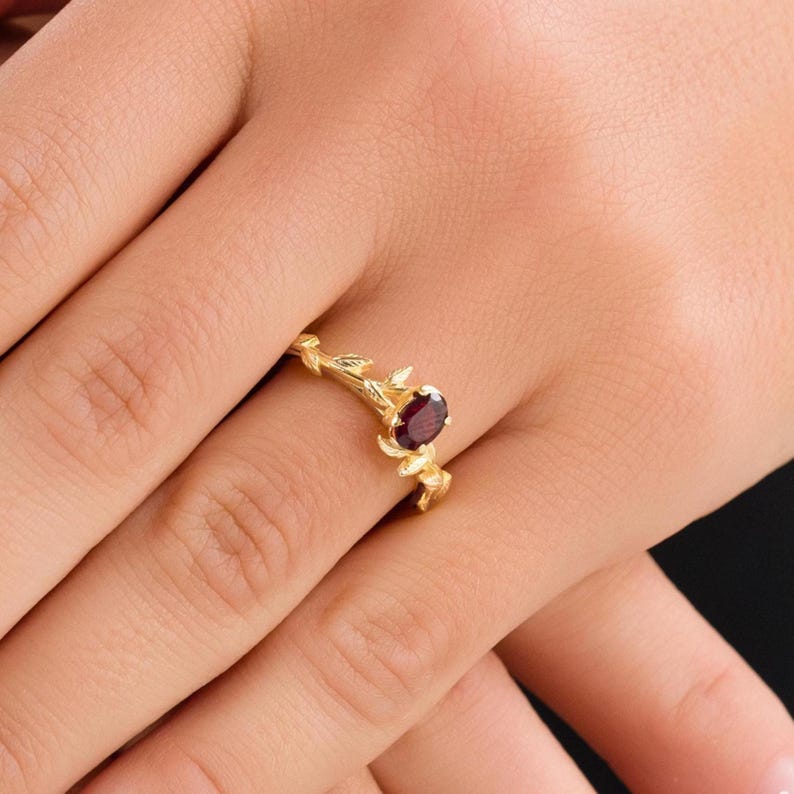 Pu&ograve; includere: Un anello d'oro con una pietra preziosa rossa incastonata in un delicato design a ramo.