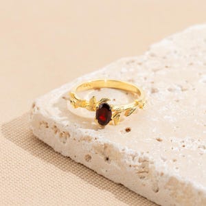 Pu&ograve; includere: Un anello d'oro con una pietra preziosa rossa incastonata in un design a foglie.