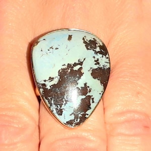 May include: A silver ring with a large, teardrop-shaped stone. The stone is a light blue color with brown and black markings.