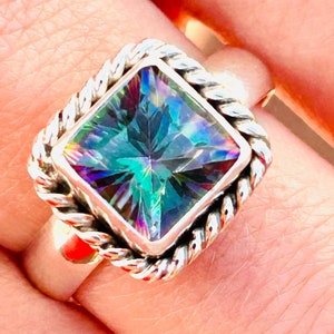 May include: A silver ring with a large, square-shaped, iridescent gemstone set in a rope-like design.