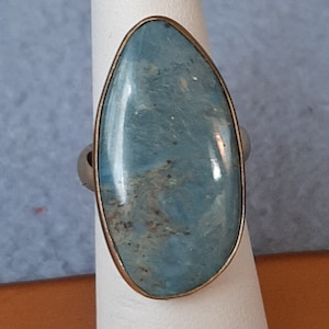May include: A ring with a large, oval-shaped blue gemstone set in a gold-toned metal band.