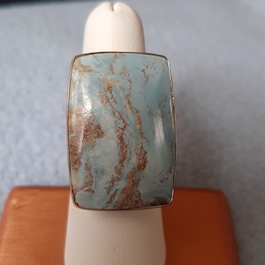 May include: A gold ring with a light blue and brown marbled stone. The stone is rectangular and has a smooth, polished finish.