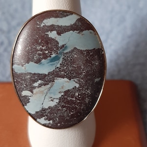 May include: A ring with a large oval-shaped stone set in a gold band. The stone is a brown and blue agate with a swirling pattern.