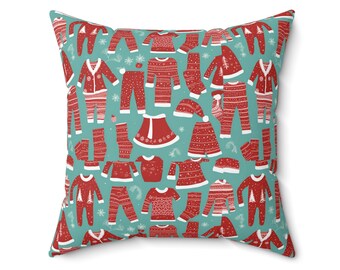 Puede incluir: Una almohada de color azul verdoso con un patrón repetido de ropa navideña roja y blanca. La ropa incluye suéteres, pantalones, vestidos y sombreros.