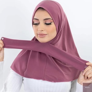 Può includere: Un hijab color malva con maniche attaccate. L'hijab è realizzato in un tessuto morbido ed elastico e presenta chiusure a scatto sulle maniche. Il prodotto è progettato per un abbigliamento modesto ed è adatto a varie occasioni.