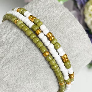 May include: A triple-strand bracelet made with green, white and gold beads. The bracelet is made with small, round beads and has a simple, elegant design.