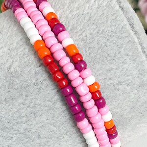 May include: A multi-coloured beaded bracelet with pink, orange, red and purple beads. The bracelet is made of small, round beads that are strung together in a repeating pattern.