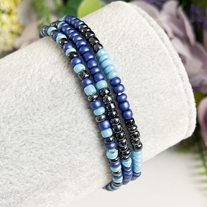 May include: A multi-strand bracelet made of blue and black seed beads. The bracelet is layered with different shades of blue beads, creating a gradient effect.