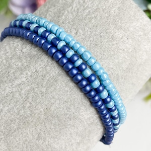 May include: A set of three beaded bracelets in shades of blue, with the darkest blue beads at the bottom and the lightest blue beads at the top.