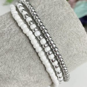 May include: Three white beaded bracelets with silver beads woven in.