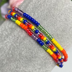 May include: Multicolored beaded bracelet with green, blue, yellow, orange, and purple beads. The bracelet is layered with multiple strands of beads.