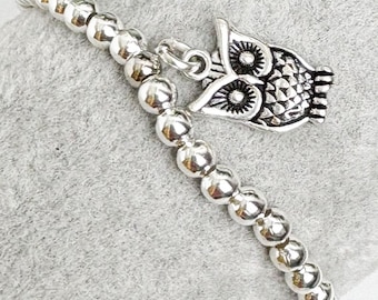 May include: Silver beaded bracelet with an owl charm. The bracelet features small, round beads strung together, with a detailed owl pendant attached. The owl charm has intricate feather detailing and large eye sockets.