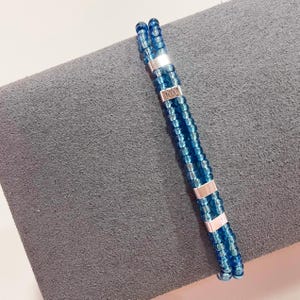 May include: A blue beaded bracelet with silver accents. The bracelet has the word "MOM" engraved on one of the silver accents.