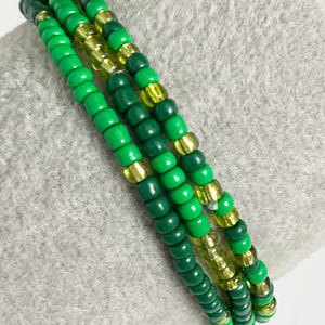 May include: A set of three green and gold beaded bracelets. The bracelets are made with small, round beads in shades of green and gold.